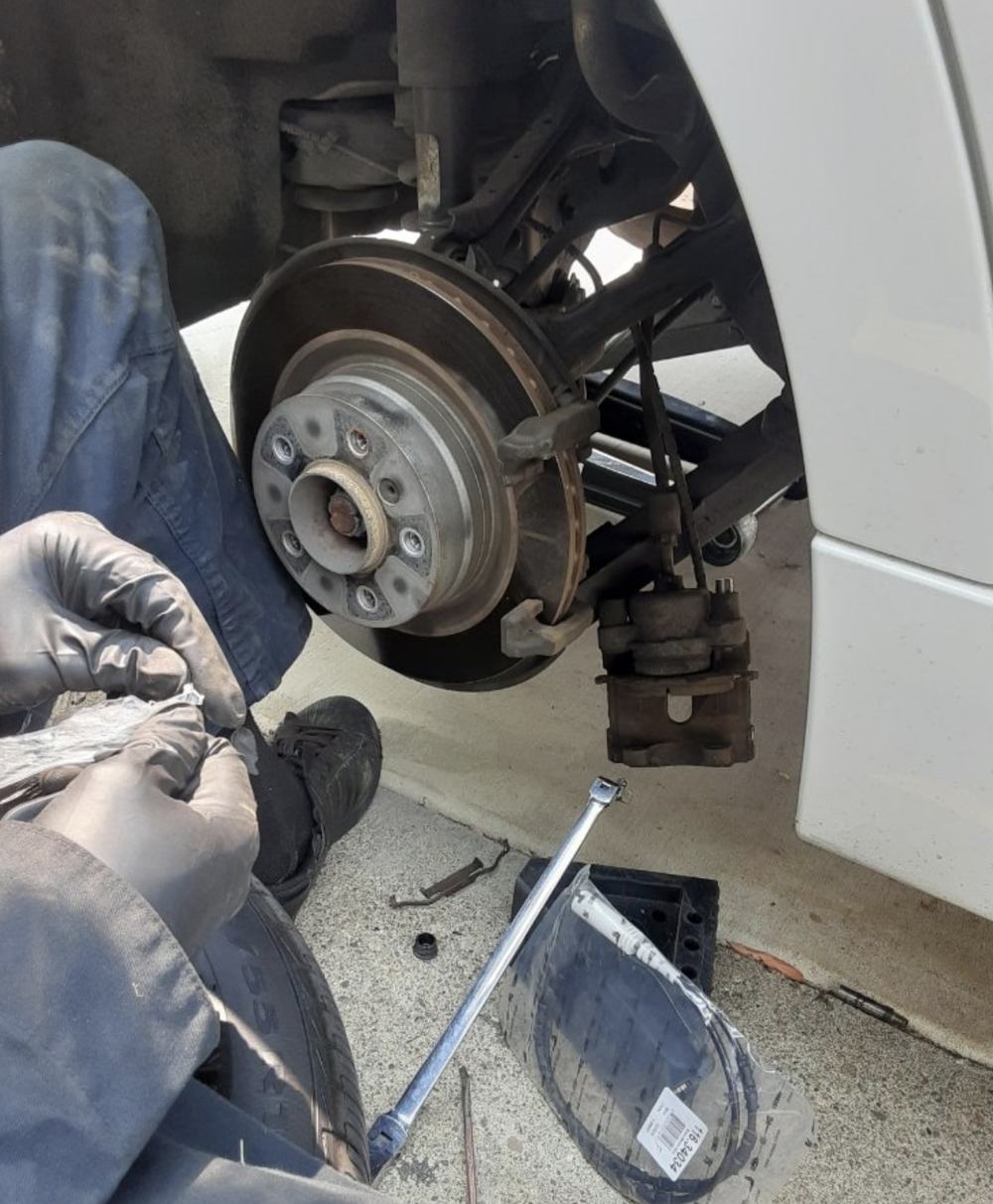 A gloved mechanic removing a worn brake rotor and caliper from a white car